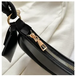 Close-up of smooth gold metal zipper and black leather puller on the crescent bag