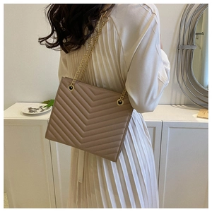 Detail of taupe quilted tote bag featuring V-shaped stitching and gold chain straps