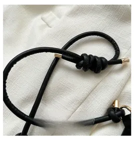 Close-up of black leather rope strap with gold metal tips and knotted detail on beige fabric