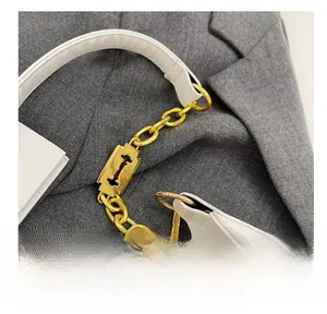 Détail du sac blanc avec bandoulière en chaîne dorée et pendentif en forme de lame de rasoir