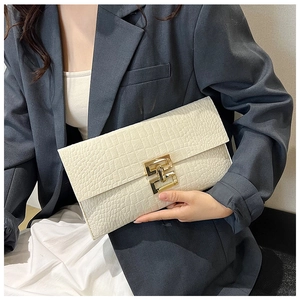 Detail of a beige crocodile embossed clutch with a prominent golden geometric clasp