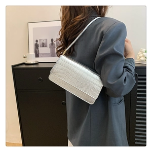 Détail du sac baguette argenté motif crocodile porté à l'épaule par un mannequin