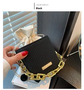 Detail view of a black woven bucket bag with thick gold chain handle on a book