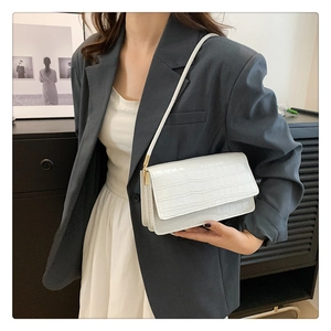 Détail d'un petit sac à bandoulière blanc à motif crocodile sur une veste grise