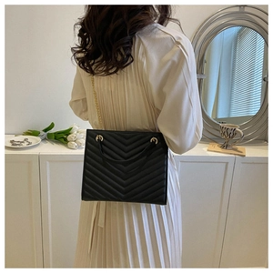 Detail of black quilted shoulder bag with gold chain strap worn with a white dress