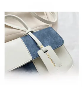 Detail van de schoudertas van wit leer en blauwe denim met gouden metalen accenten