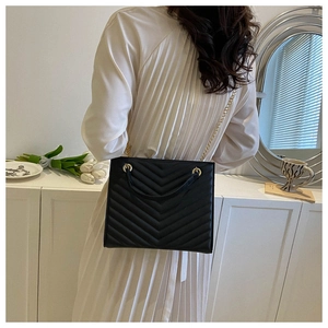 Lifestyle shot of black V-quilted tote bag featuring gold chain and sleek leather strap