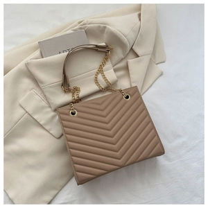 Macro shot of brown V-quilted texture with gold chain strap on a chic tote bag