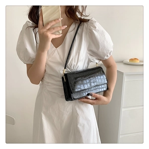 Détail de la texture croco noir sur un sac à bandoulière rectangulaire à rabat