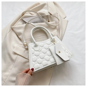 Detail of white quilted trapezoid handbag with gold hardware and mini charm bag on a blazer