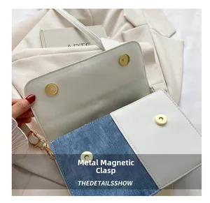 Detail van de gouden magnetische sluiting op een tas van blauwe denim en wit leer