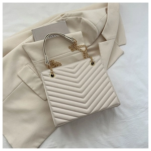 Close-up of beige quilted tote bag with V-shaped stitching and gold chain strap