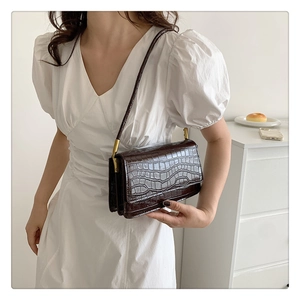 Détail du sac sous le bras marron foncé effet crocodile avec fermoir et fine bandoulière
