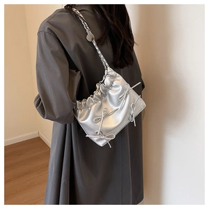 Close-up of silver pleated bucket bag featuring metallic bows and chain strap details