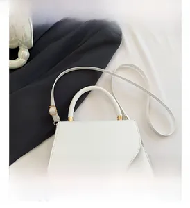 Dettaglio borsa a trapezio bianca con hardware dorato e patta asimmetrica curva