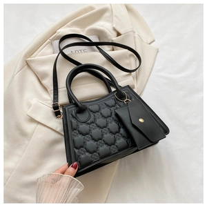 Detail of black embossed crossbody bag with gold hardware on beige blazer background