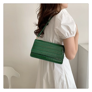 Détail du sac à bandoulière vert foncé texture crocodile porté sur robe blanche