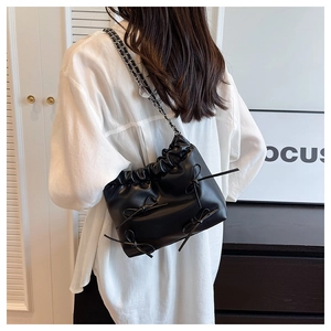 Detail of black ruched bucket bag with delicate bow accents and silver chain strap