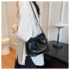 Detail of a black pleated bucket bag with bow accents and a silver metal chain strap