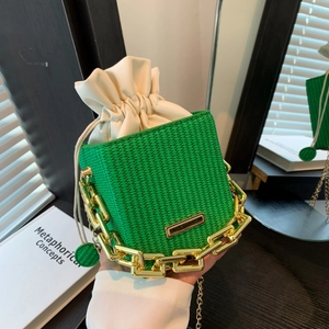 Green woven bucket bag with gold chain handle and drawstring closure in a modern setup