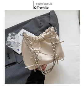 Detail of cream pleated handbag with bow accents and metal chain strap on minimalist background