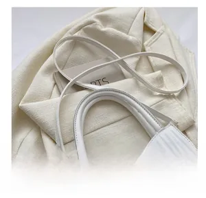 Detail van witte gewatteerde schoudertas met gouden hardware op een tweed jasje