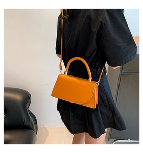 Detail shot of bright orange leather handbag showing shoulder strap and handle on a model