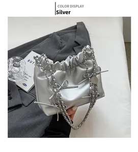Silver bow tote bag with metallic leather and chain strap against a grey blazer