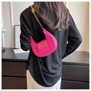 Détail du sac croissant rouge rose avec chaîne dorée porté par un mannequin élégant