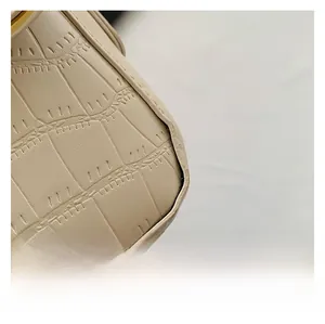 Macro detail of beige crocodile embossed leather and fine stitching on a small square bag