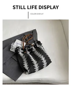 Detail of black and white woven bucket bag with frayed edges and brown leather handles