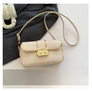 Close-up of cream textured faux-crocodile shoulder bag with gold metal clasp and phone for scale