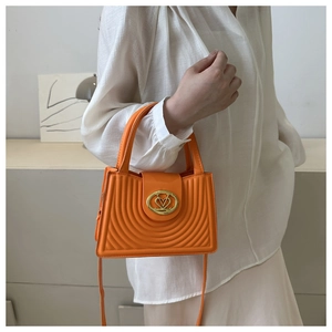 Detail of bright orange handbag featuring semi-circular sunburst texture and heart clasp