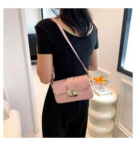 Detail of pink croc-textured crossbody bag with golden clasp worn by a model