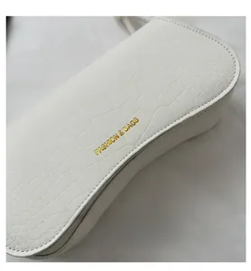 Gros plan sur la texture crocodile blanc et le logo doré du sac à bandoulière chic