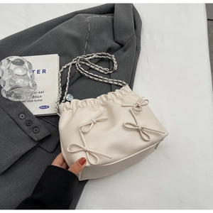 Detail of creamy white bucket bag featuring bow accents and pleated drawstring closure