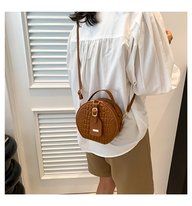 Detail of round brown crossbody bag featuring quilted texture and golden hardware