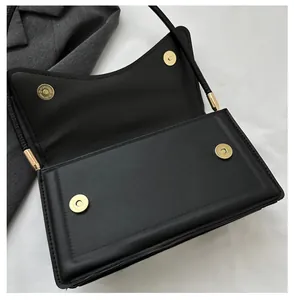 Detail of minimalist black bag showing double magnetic gold clasps on matte leather flap