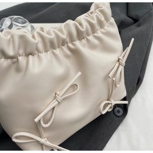 Detailed view of cream pleated bucket bag featuring elegant ribbon bow accents