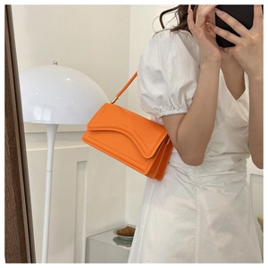Chic orange faux leather underarm bag with wave flap detail worn as a shoulder bag