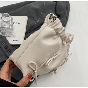 Detail of a beige drawstring bucket bag with pleated design and a delicate bow accent
