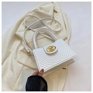 Detail of white quilted handbag with gold logo on beige blazer and decorative card