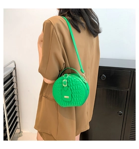 Detail of round green crossbody bag with crocodile texture and metal buckle accents