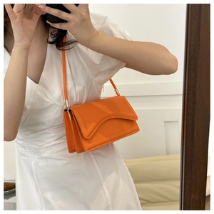 Detail of a bright orange crossbody bag featuring a unique wavy flap and gold hardware