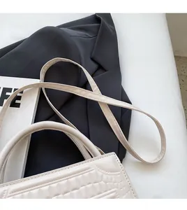 Detail of cream crossbody bag with crocodile texture and slim shoulder strap