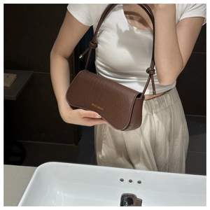 Détail du sac en cuir marron foncé à motif crocodile avec bandoulière à nœud et logo