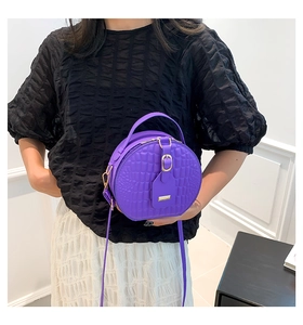 Dettaglio borsa rotonda viola motivo coccodrillo con finiture dorate e targhetta