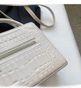 Detail of cream white quilted handbag featuring square texture and metallic zipper