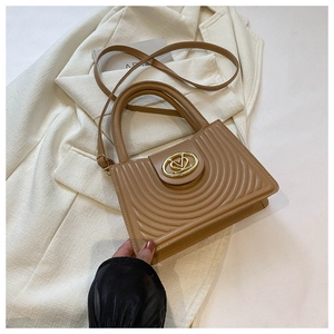 Detail of camel PU leather handbag with circular metal logo and curved stitching texture