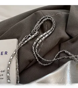 Détail de la bandoulière en chaîne argentée entrelacée de cuir sur fond en tissu brun